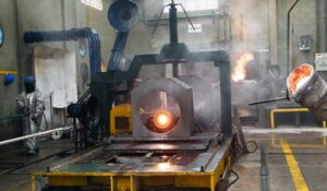 Interior de fundição com metal incandescente sendo vazado em molde, operadores protegidos e máquinas industriais; processo típico da TCINOX com controle e alta precisão metalúrgica.