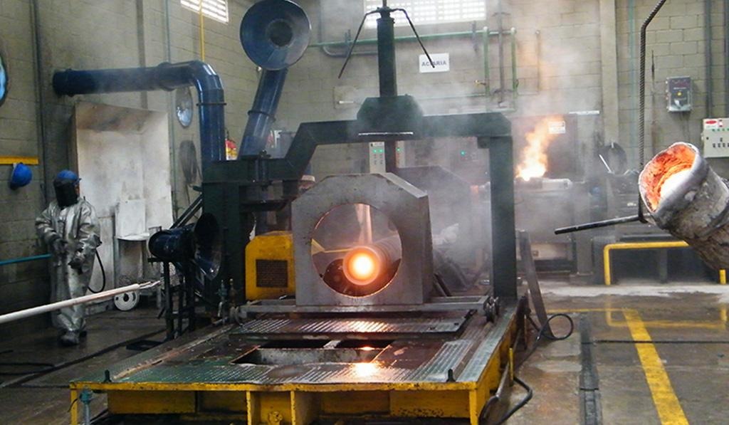 Interior de fundição com metal incandescente sendo vazado em molde, operadores protegidos e máquinas industriais; processo típico da TCINOX com controle e alta precisão metalúrgica.